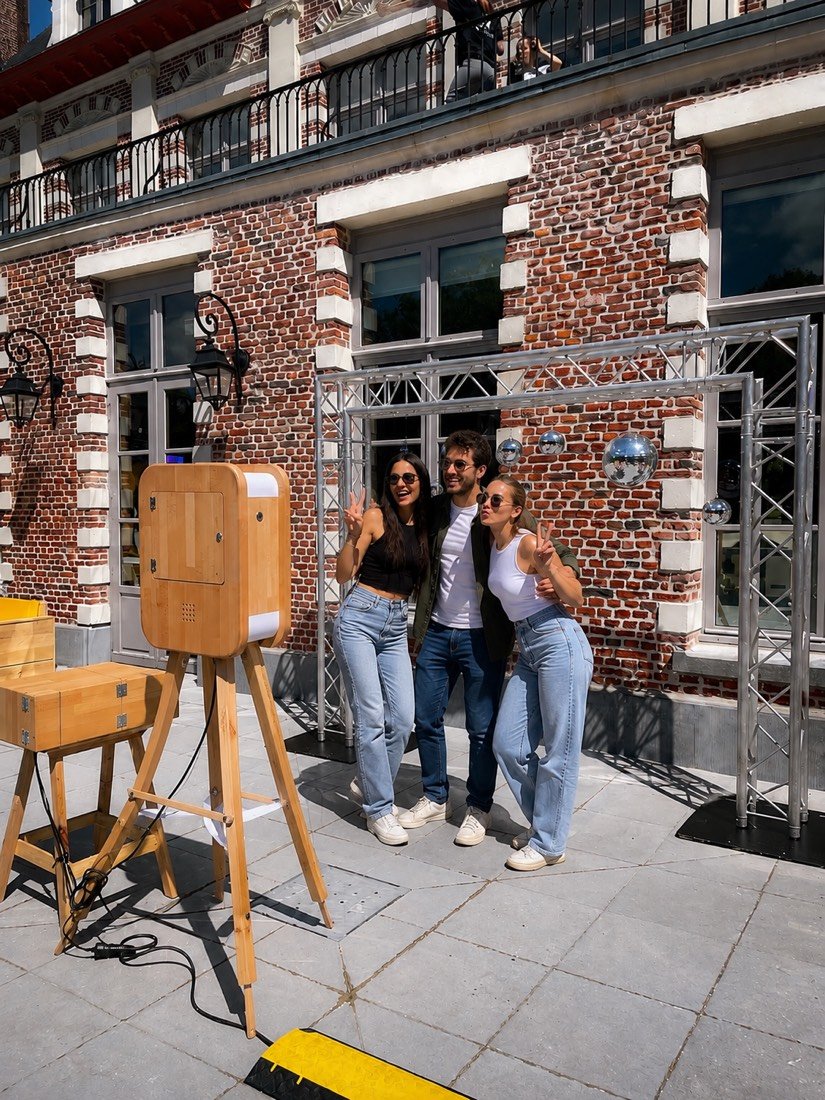 Invités posant à côté d’une borne photo Kapsule devant une façade en briques